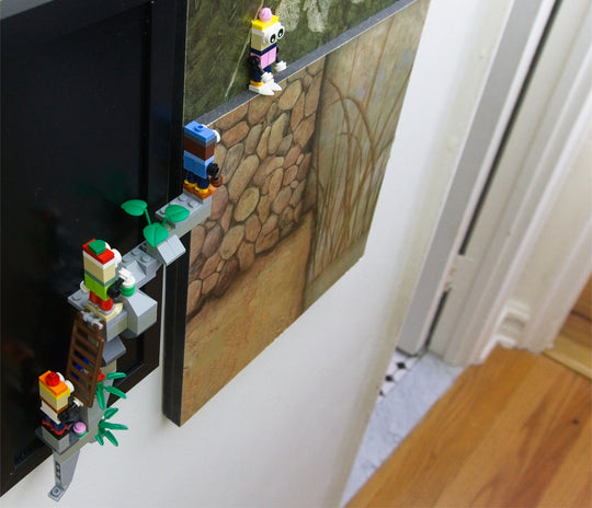 Characters made with LEGO ® blocks and supported by MBRIKS magnetic construction blocks climb onto a wall-mounted painting.  